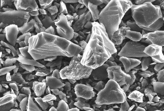 Microscopic image of mineral particles showcasing various shapes and sizes, with a scale bar indicating 50 micrometers. This high-resolution scanning electron microscope (SEM) image highlights the texture and structure of the samples, useful for geological or materials analysis.