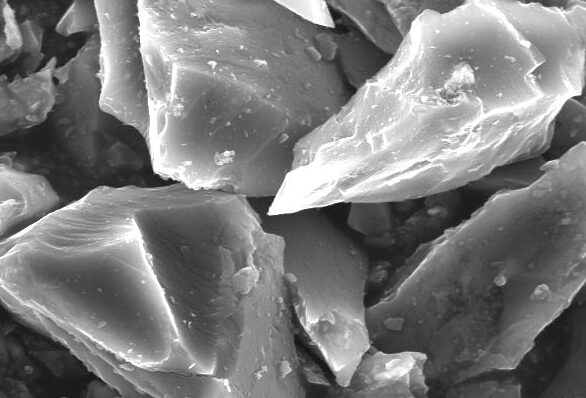 Microscopic image of crystalline silicon fragments, showcasing angular shapes and varied textures, with a scale bar indicating a measurement of 10 micrometers.