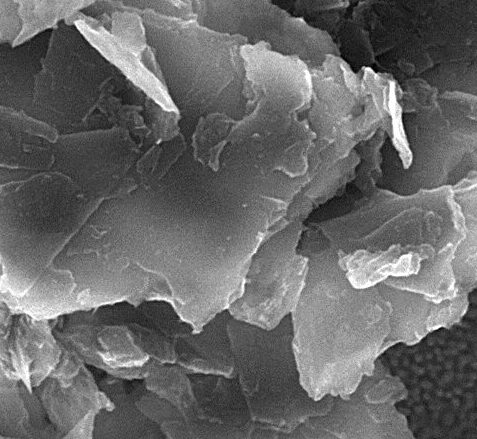 High-resolution scanning electron microscope image of layered mineral flakes, showcasing their surface texture and structure at a magnification of 184,887x. The scale bar indicates a size of 500 nanometers, highlighting the fine details of the material's morphology.