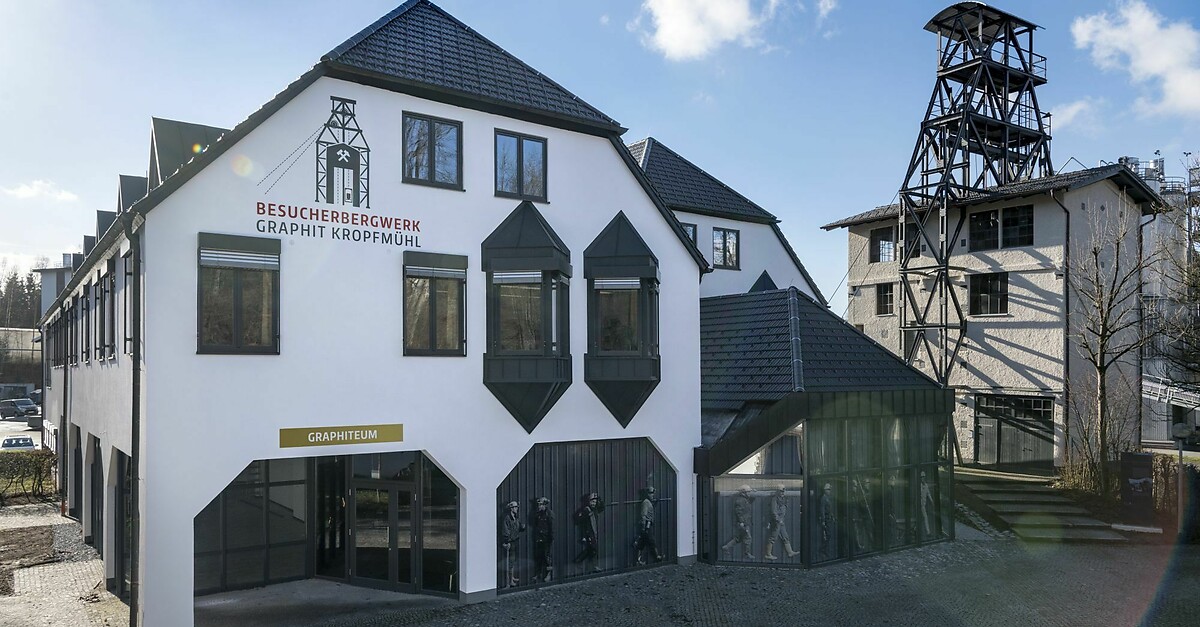 Visitor center of the Graphit Kropfmühl graphite mine, featuring modern architecture, large windows, and a prominent mining tower in the background. The building includes the "Graphitheum" exhibit, showcasing the history and significance of graphite mining.
