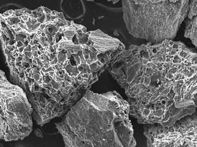 Scanning electron microscope image showing detailed textures of mineral particles, highlighting their irregular shapes and surface features at a magnification of 50x.
