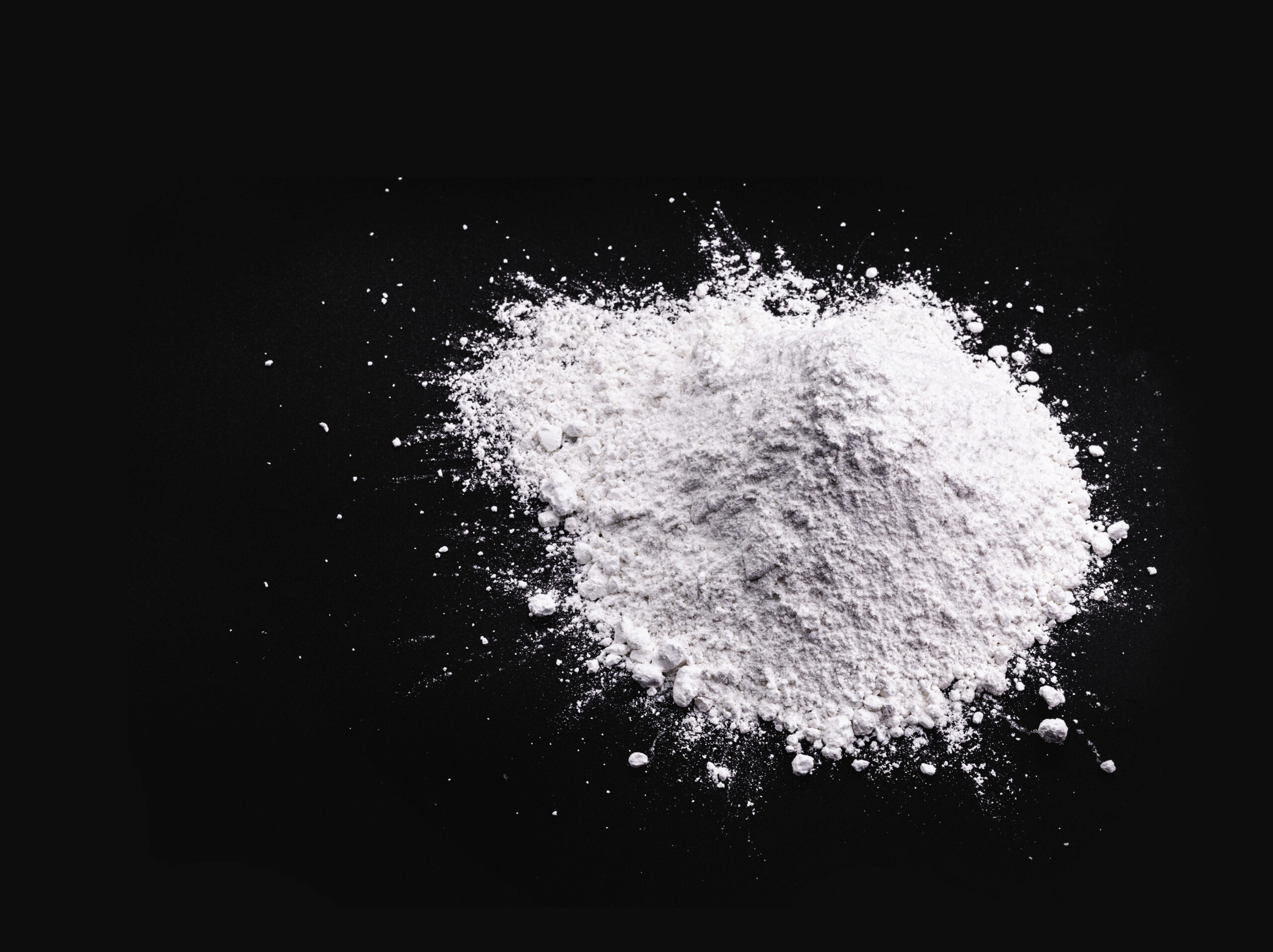 White powdery substance piled on a black background, commonly used in baking and cooking, possibly flour or sugar, showcasing its fine texture and versatility in various recipes.
