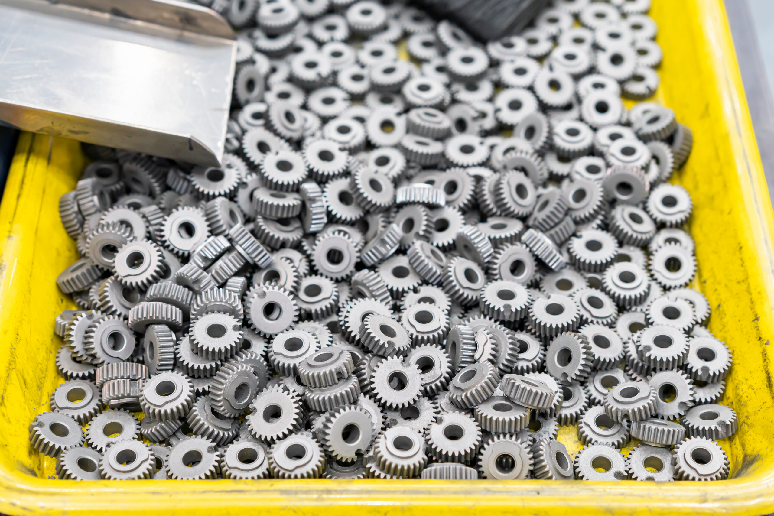 Close-up of a yellow tray filled with numerous small, gray metal gears, showcasing their intricate details and uniform design. Ideal for industrial applications and mechanical engineering.