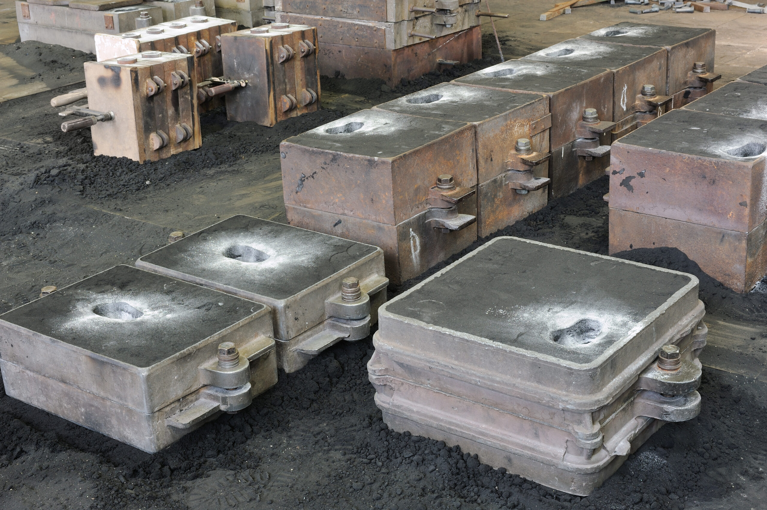Industrial metal casting molds arranged on a workshop floor, surrounded by black sand, showcasing various shapes and sizes used for manufacturing processes.