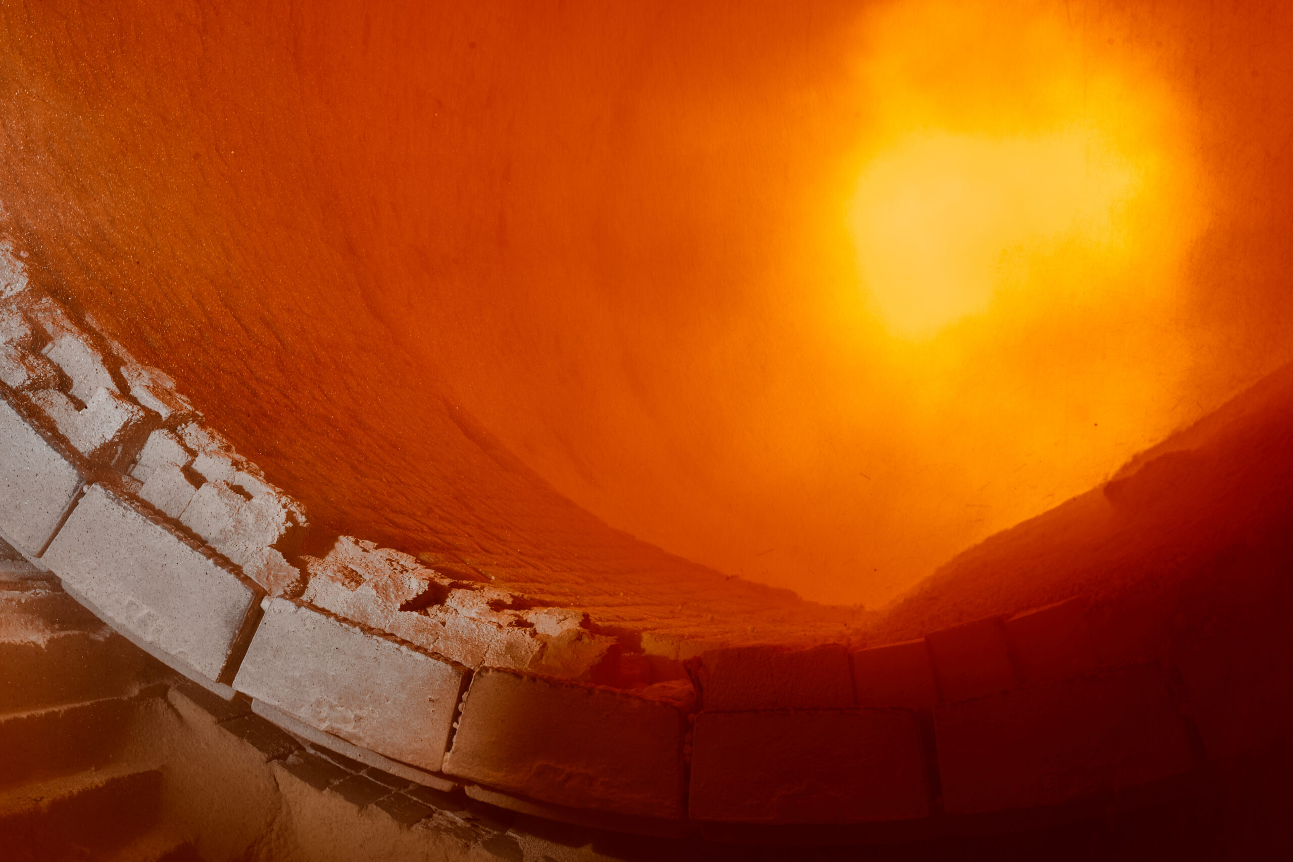 Interior view of a furnace with glowing orange heat emanating from the center, showcasing the brick structure and texture of the walls, emphasizing high-temperature industrial processes.