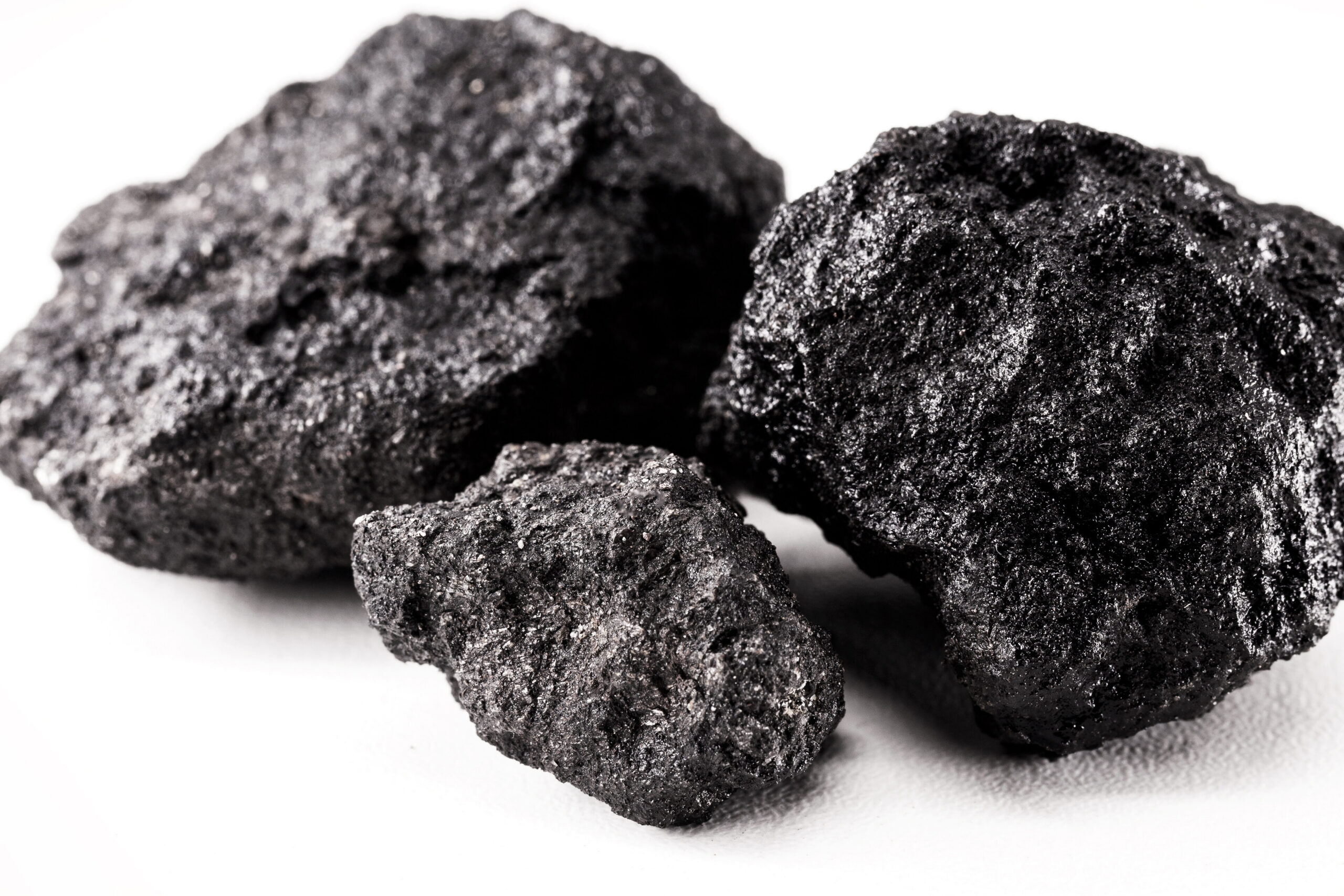 Close-up image of three pieces of black coal on a white background, showcasing the rough texture and natural formation of the coal. Ideal for discussions on fossil fuels, energy resources, or geology.