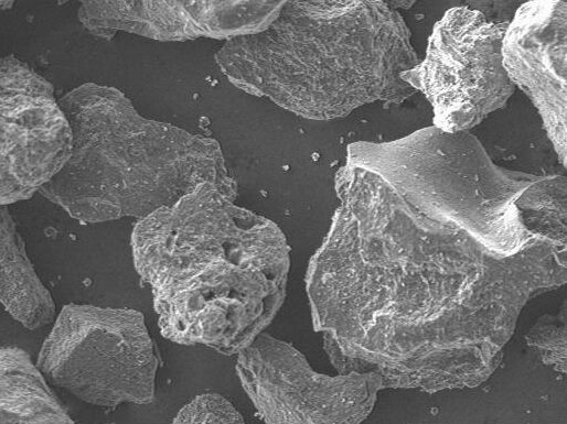Scanning electron microscope image showing a close-up view of various mineral particles, highlighting their irregular shapes and textures at a magnification of 50x.