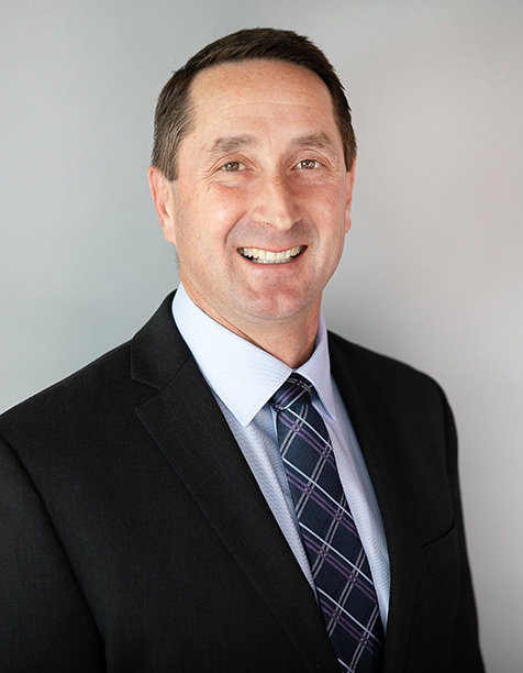 Smiling professional man in a business suit with a tie, standing against a neutral background, conveying confidence and approachability. Ideal for corporate profiles or business-related content.