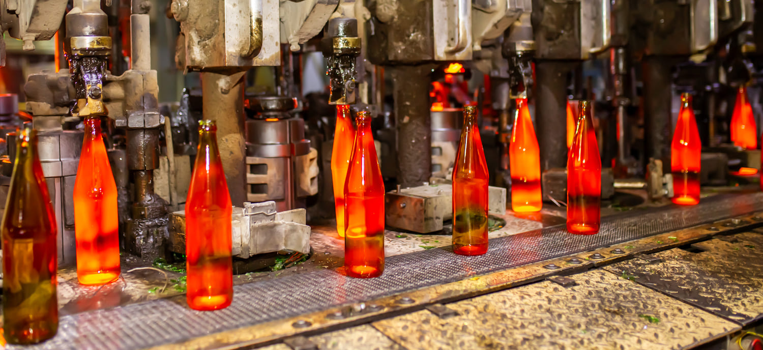 Production line of amber glass bottles in a manufacturing facility, showcasing automated machinery and the bottling process with vibrant orange hues.