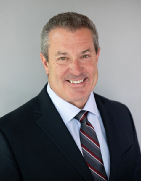 Professional headshot of a smiling man in a dark suit and striped tie, set against a neutral background, representing confidence and approachability in a business context.