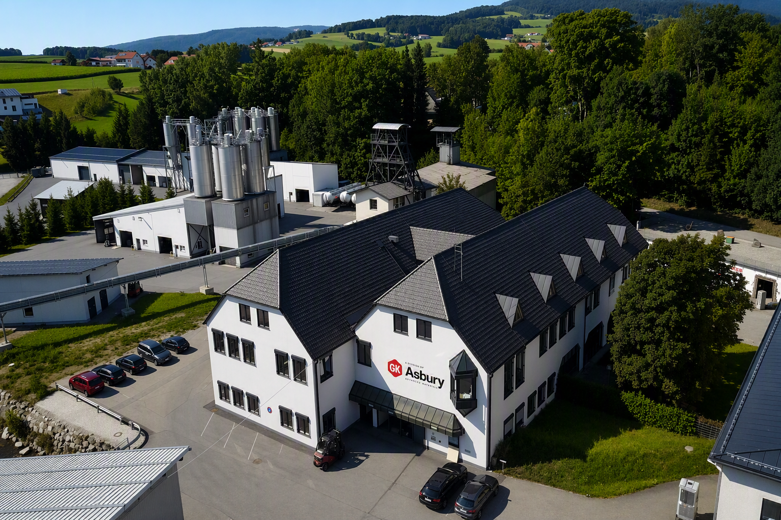 Aerial view of the Asbury Advanced Materials facility, showcasing the main building with the Asbury logo, adjacent production structures, and surrounding greenery, in the context of the Graphit Kropfmühl GmbH acquisition announcement.