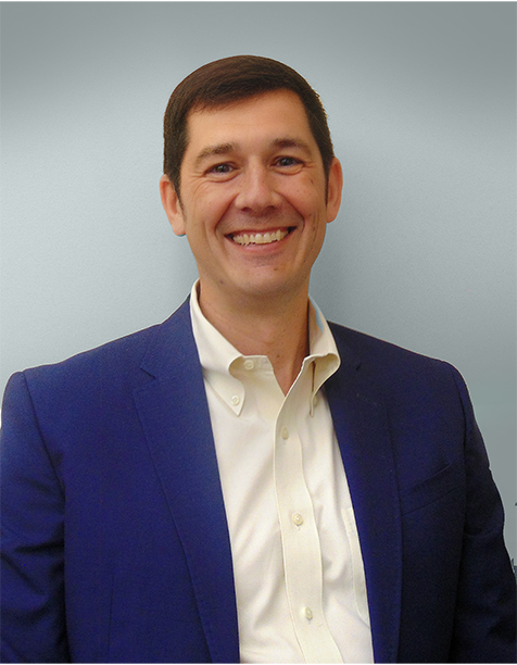 Smiling man in a blue blazer and white shirt against a light gray background, representing professionalism and approachability in a business setting.