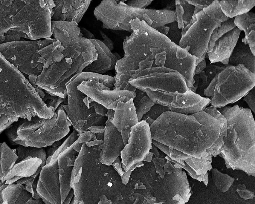 Scanning electron microscope image showing a close-up view of layered materials with a focus on angular, flake-like structures. The image is captured at 5,000x magnification, highlighting the intricate details of the surface morphology at a scale of 1 micrometer.