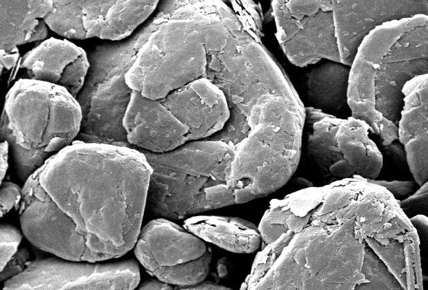 Scanning electron microscope image of mineral particles, showcasing a variety of shapes and sizes. The scale bar indicates a measurement of 50 micrometers, highlighting the fine detail of the sample's surface texture. Ideal for studies in geology and materials science.