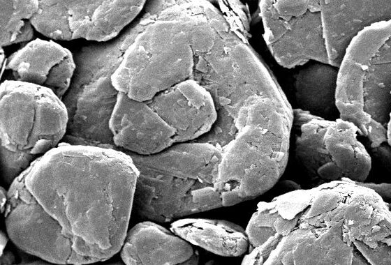 Scanning electron microscope image of mineral particles, showcasing a variety of shapes and sizes. The scale bar indicates a measurement of 50 micrometers, highlighting the fine detail of the sample's surface texture. Ideal for studies in geology and materials science.