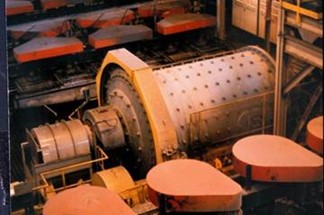 Industrial ball mill used for grinding materials in a manufacturing facility, featuring a large cylindrical drum and multiple orange hoppers in the background.