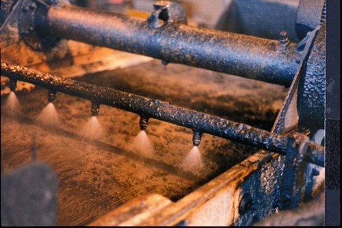 Industrial processing of natural flake graphite, showcasing a close-up of a machinery component with water mist nozzles. The image highlights the equipment used in the production and refining of graphite flakes.