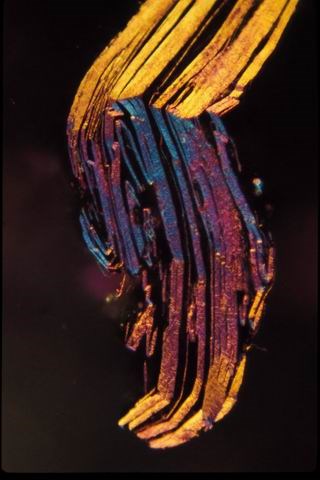 Close-up image of a colorful crystal structure displaying vibrant blue, yellow, and orange hues, showcasing layered formations and intricate details under polarized light. Ideal for studies in mineralogy and crystallography.