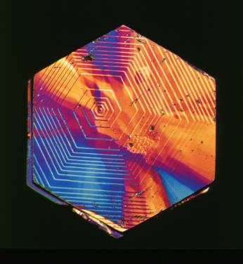 Hexagonal crystal structure displaying vibrant colors and intricate patterns under polarized light, showcasing the unique optical properties of the material.