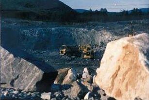 Heavy machinery operates in a rocky quarry surrounded by large boulders and hills, showcasing the extraction process in a mining environment.