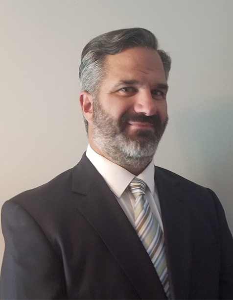 Professional man in a business suit with a tie, smiling confidently against a neutral background.