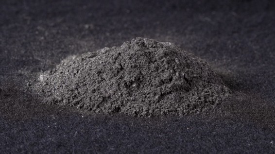 Fine gray powder on a dark surface, possibly representing a mineral or industrial material, showcasing its texture and granularity.
