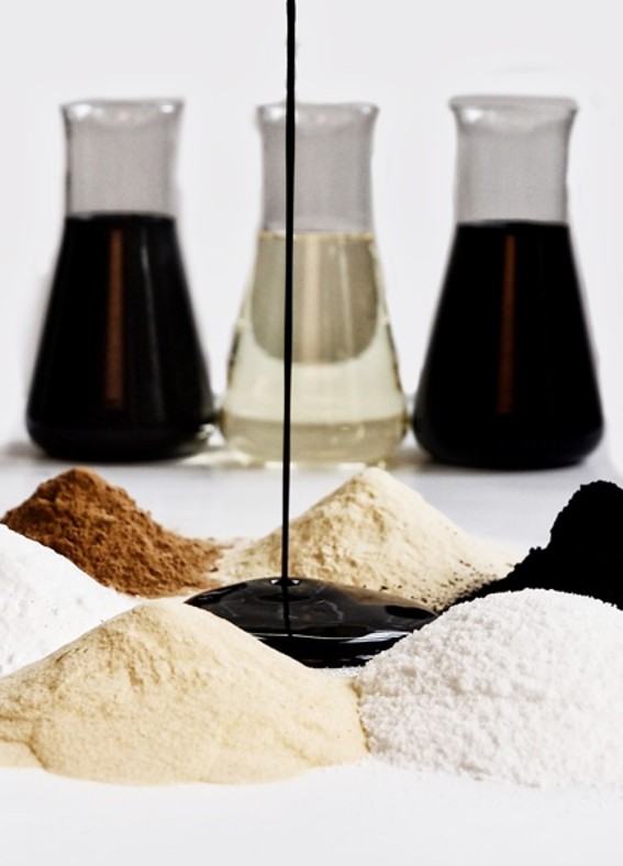 Assorted powders in various colors arranged in mounds with a dark syrup pouring in the center, flanked by three glass containers of different liquid colors, showcasing ingredients for baking or cooking.