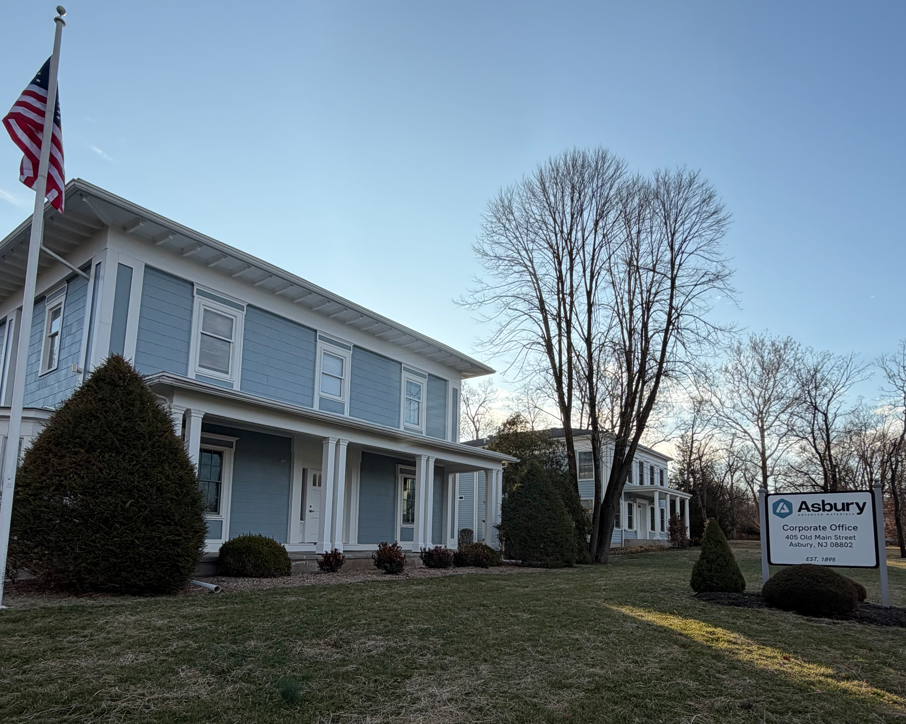 Exterior view of Asbury Corporate Office building with American flag, located at 405 Old Main Street, Asbury, NJ. The image showcases the building's architecture and surrounding landscaping, emphasizing a professional and welcoming atmosphere.