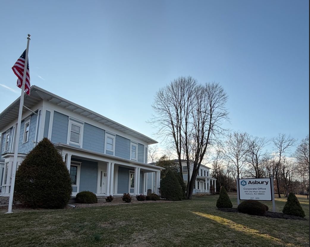 Exterior view of Asbury Corporate Office building with American flag, located at 405 Old Main Street, Asbury, NJ. The image showcases the building's architecture and surrounding landscaping, emphasizing a professional and welcoming atmosphere.