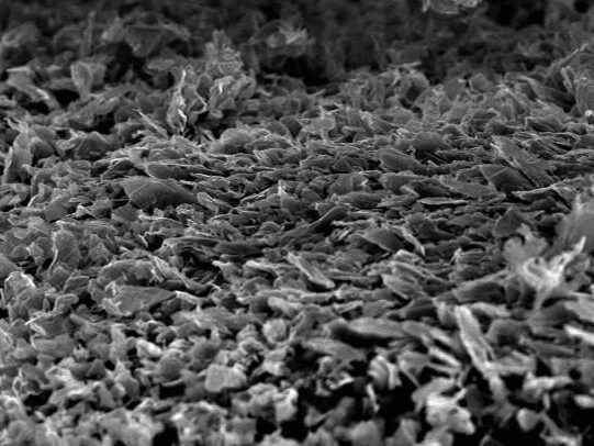 Scanning electron microscope image showing a textured surface at 680x magnification, revealing intricate layers and structures on a material sample. The scale bar indicates a size of 10 micrometers, highlighting the fine details of the surface morphology.
