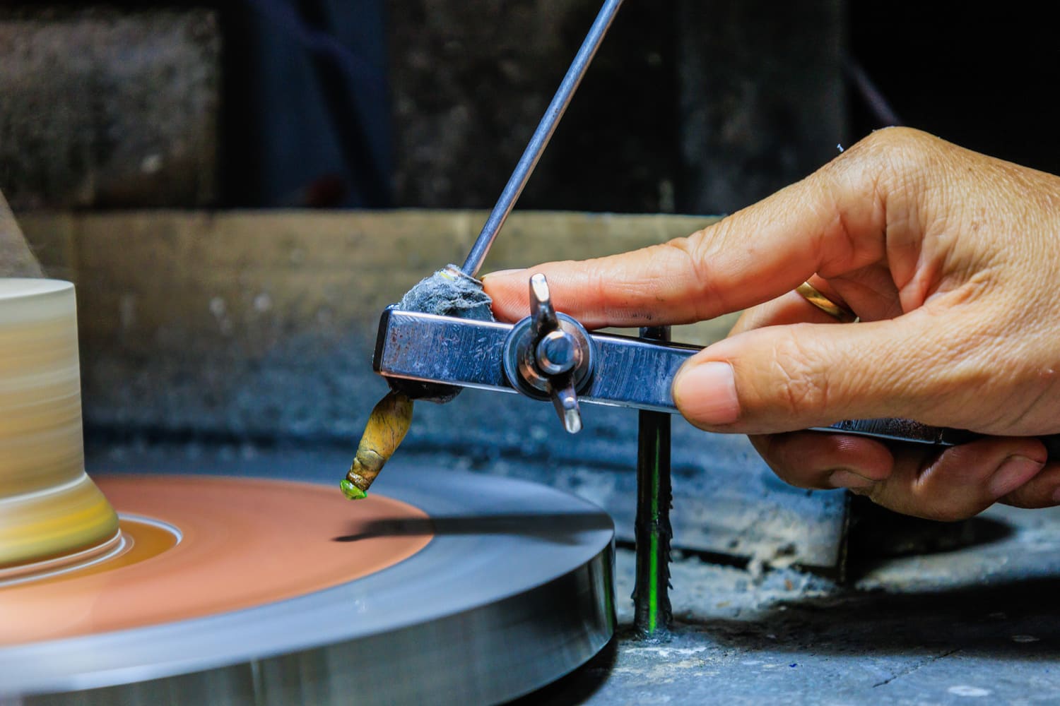 Close-up of a hand using a compass to measure and shape a pottery piece on a spinning wheel, showcasing the craftsmanship involved in pottery making. The image highlights the precision tools and techniques used in traditional ceramics.
