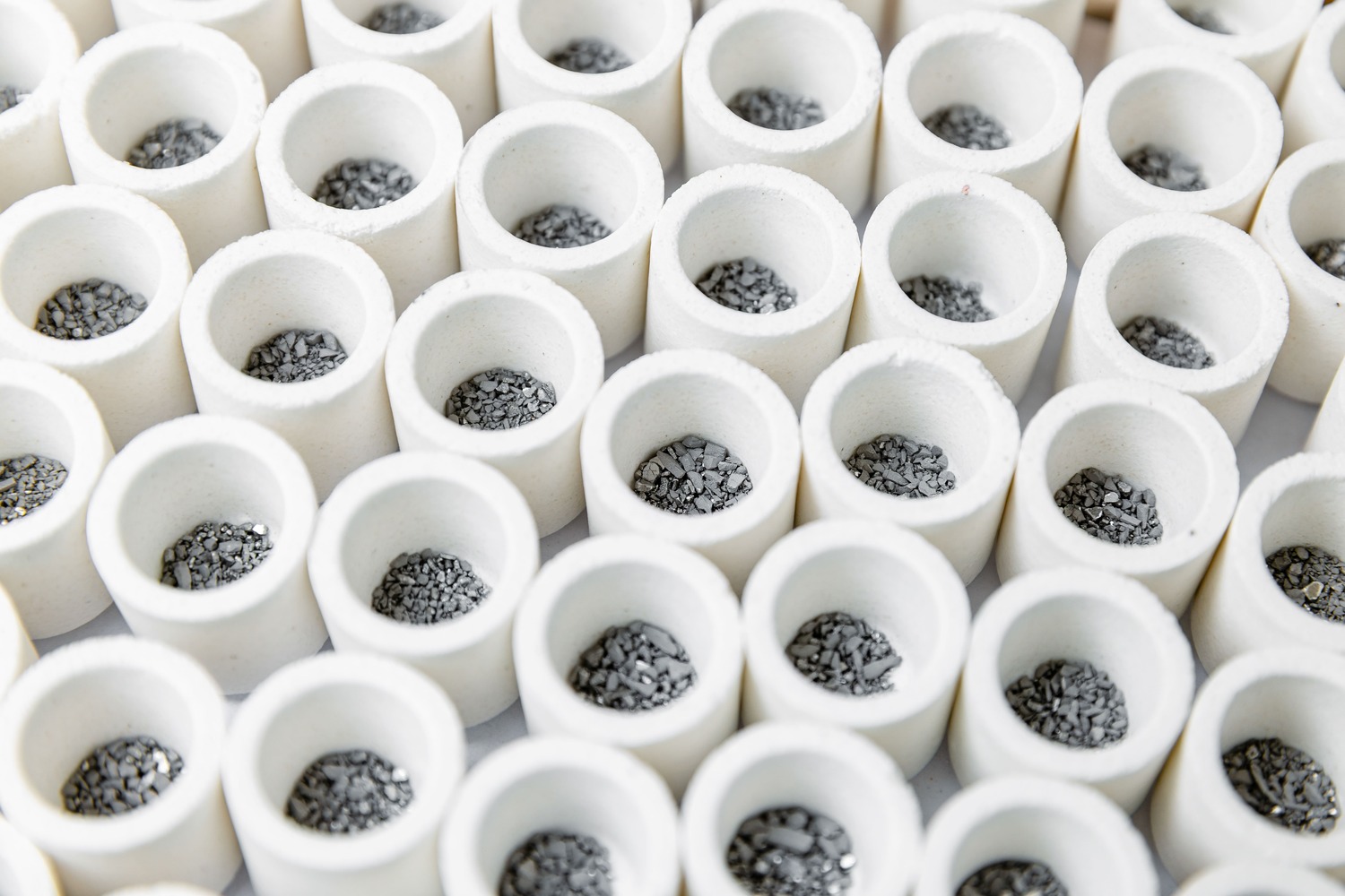 Close-up view of multiple white ceramic crucibles filled with small pieces of gray material, commonly used in laboratory settings for chemical reactions and material analysis.