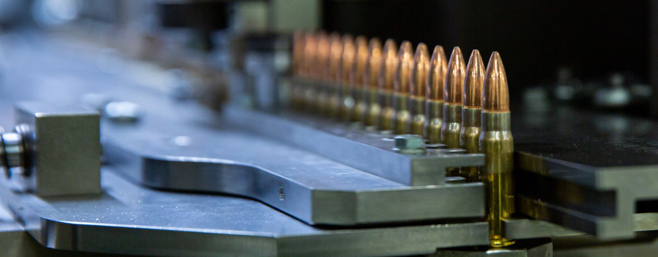 Close-up of a precision machinery assembly line featuring rows of copper-tipped bullets on a metal conveyor, highlighting the manufacturing process in the ammunition industry.