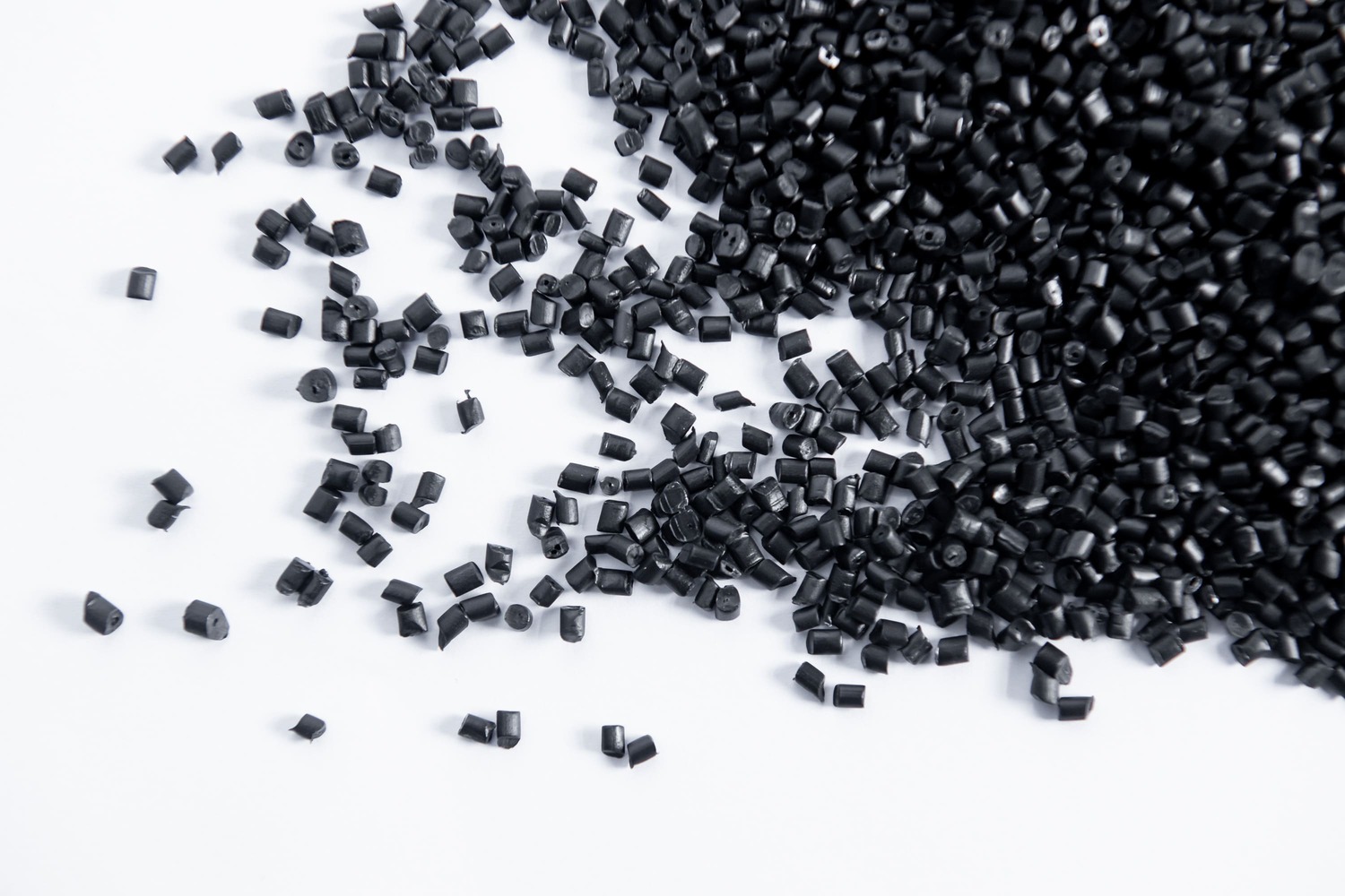 Black plastic pellets scattered on a white surface, commonly used in manufacturing and industrial applications.