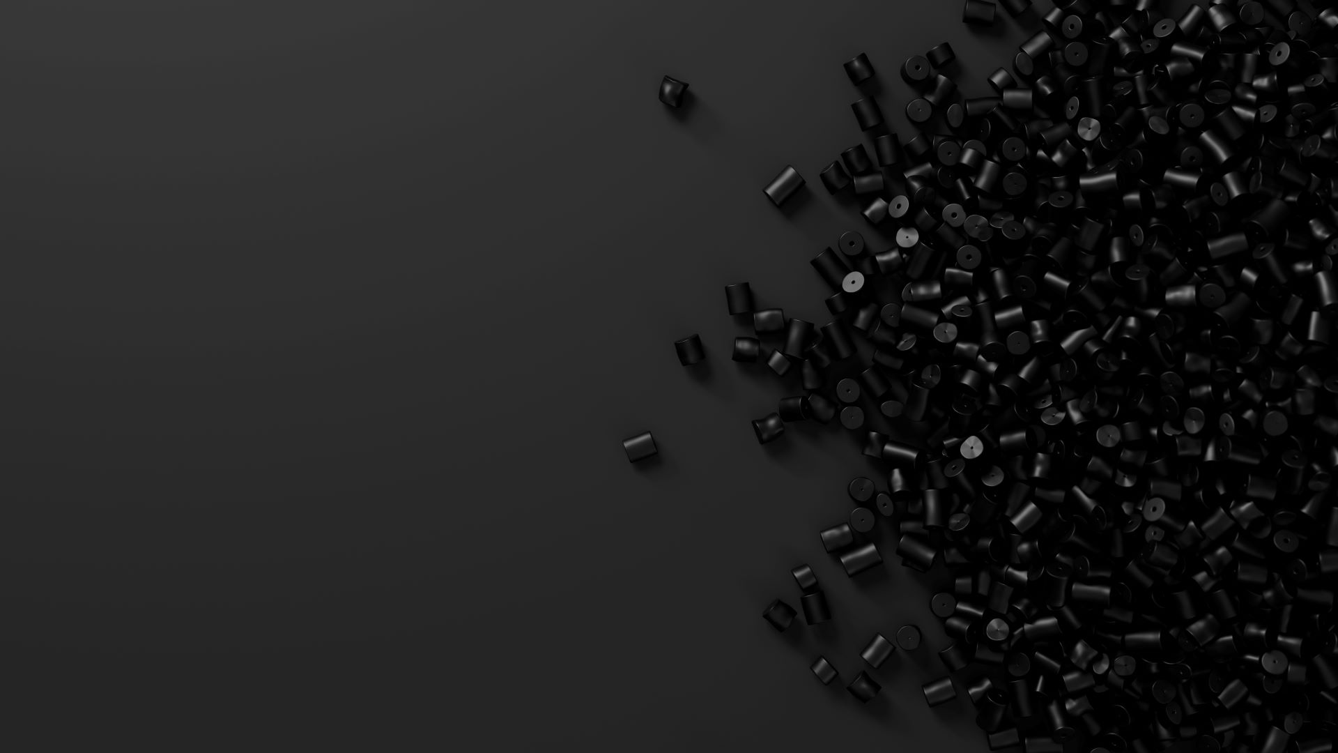 Black plastic pellets scattered across a dark surface, showcasing various shapes and sizes, commonly used in manufacturing and production processes.