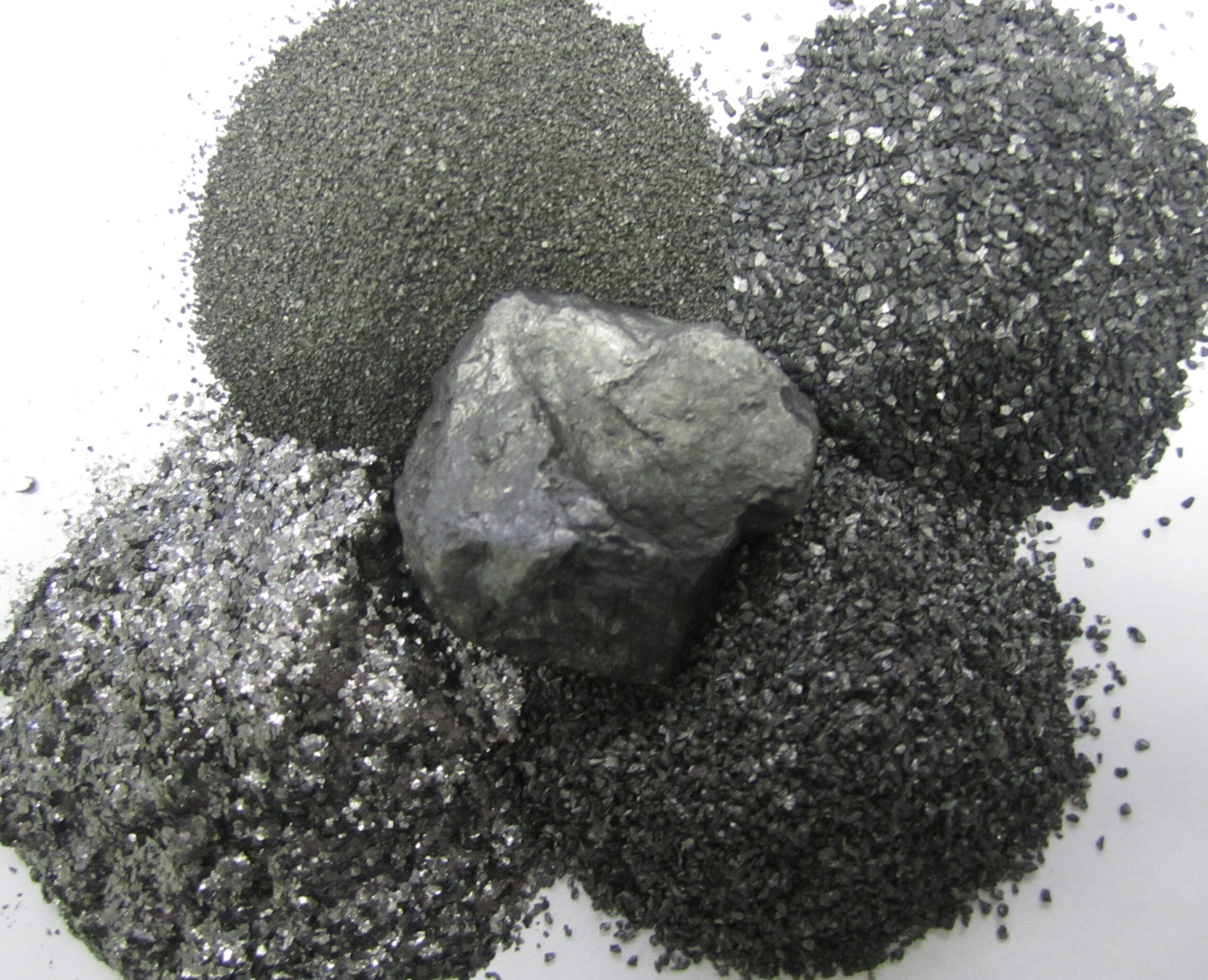 Various types of black mineral powders and a larger rock piece, showcasing different textures and sizes of minerals, ideal for industrial applications and material science.