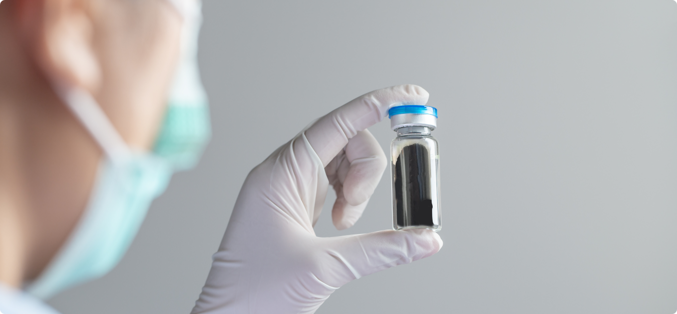 A healthcare professional in a white glove holds a small glass vial with a blue cap, containing a dark liquid, against a neutral background, emphasizing its potential medicinal use.